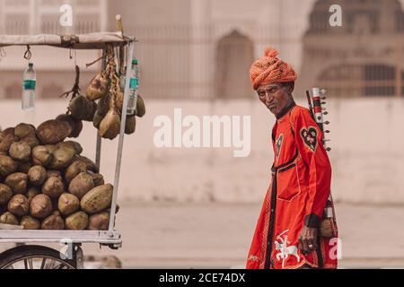 Indien - 2. November 2012: Seitenansicht eines älteren männlichen Musikers mit traditionellem Musikinstrument und Turban, der in der Stadt steht und in die Kamera schaut Stockfoto