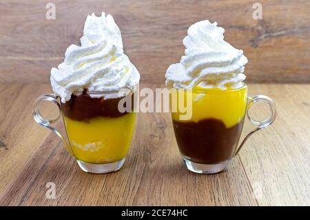 Gelbe Vanille- und Schokoladencreme mit Schlagsahne im Glas Tassen auf Holztisch Stockfoto