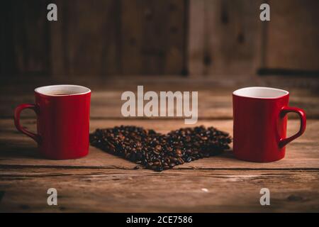 Keramikbecher mit Heißgetränk auf Holztisch mit platziert Körner in Herzform angeordnet Stockfoto