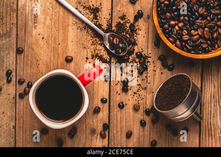 Draufsicht auf köstliche Getränke in Becher auf dem Tisch platziert Mit Kaffeebohnen und gemahlenem Kaffee im Metallfilter Stockfoto