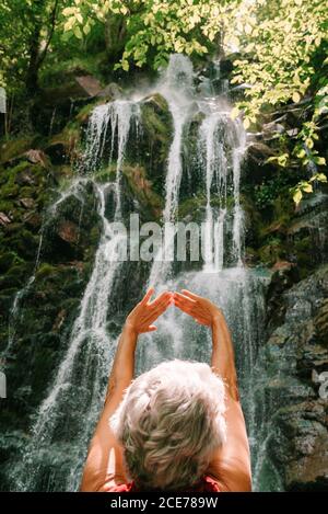 Rückansicht der nicht erkennbaren weiblichen Touristen bewundern majestätische Landschaft Wasserfall und genießen Sie die Freiheit mit erhobenen Armen während der Sommerferien Stockfoto