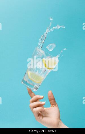 Nicht erkennbare weibliche werfen Glas von frischem Wasser mit Eis und Zitrone auf hellblauem Hintergrund zeigt Konzept der Ernährung Stockfoto