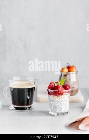 Glas Tasse Kaffee mit Chia Pudding garniert mit Himbeeren Und weiße Kirschen mit Weizen Knäckebrot mit Nussaufstrich und Marmelade mit Mandelstücken Stockfoto