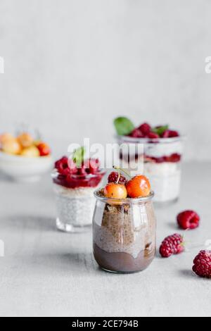 Zusammensetzung von köstlichen Puddings aus Chia Samen Joghurt gekrönt Mit Himbeerkonfitüre und Kirsche in Gläsern auf grau Tabelle Stockfoto