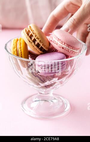 Crop weiblich unter bunten leckeren Macarons aus Glas Schüssel platziert Auf dem Tisch in der Küche Stockfoto