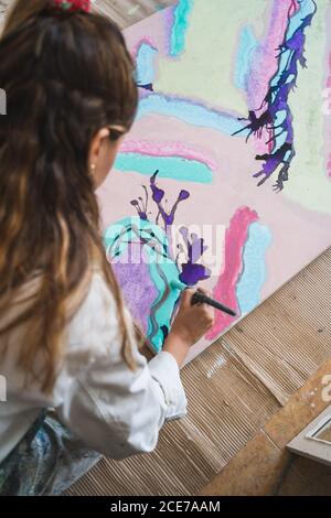 Fröhlich barfuß Künstlerin in schmutziger Robe und Handschuhe liegen Auf Holzboden mit geschlossenen Augen vor abstraktem Malerei im Kunststudio Stockfoto