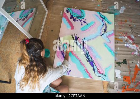 Fröhlich barfuß Künstlerin in schmutziger Robe und Handschuhe liegen Auf Holzboden mit geschlossenen Augen vor abstraktem Malerei im Kunststudio Stockfoto