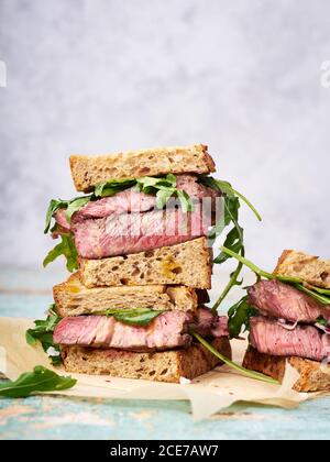 Nahaufnahme eines Stapels Rindersteak Sandwich mit Rucola und Senf Dressing vor hellem Hintergrund Stockfoto