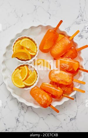 Hausgemachte, saftige, orangefarbene Eiszapfen. Auf einen weißen Teller mit Eiswürfeln gestellt Stockfoto