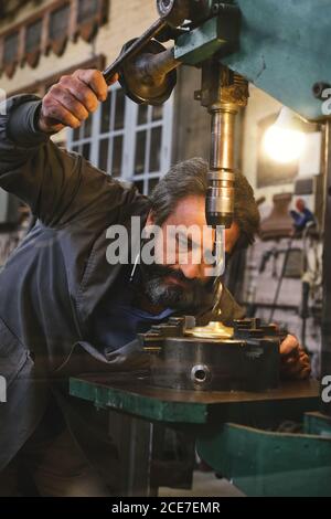 Ernte von konzentrierten mittleren Alters ernsthafte Handwerker in Uniform mit Graviermaschine während der Arbeit mit Metall im Studio Stockfoto