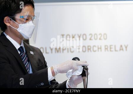 Tokio, Japan. August 2020. Ein Mitarbeiter mit Gesichtsschutz und Gesichtsmaske reinigt das Mikrofon, um die Ausbreitung des neuen Coronavirus während der Ausstellungszeremonie für die Olympische Flamme im Japanischen Olympischen Museum zu verhindern. Vertreter des Organisationskomitees der Olympischen und Paralympischen Spiele in Tokio (Tokio 2020) und des Japanischen Olympischen Komitees nahmen an der Zeremonie für die olympische Flamme Teil, bevor sie vom 1. September bis zum 1. November im Japanischen Olympischen Museum öffentlich gezeigt wurden. Quelle: Rodrigo Reyes Marin/ZUMA Wire/Alamy Live News Stockfoto