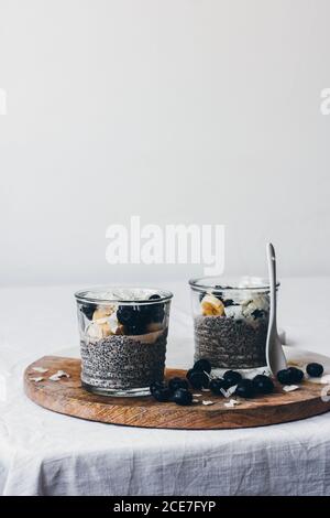 Glas Gläser mit köstlichen Chia Puddings aus frischen lecker Mandelmilch und Chiasamen mit Honig gekrönt mit Brombeeren Und Bananenscheiben auf Holzbrett vor weißem Hintergrund serviert Stockfoto