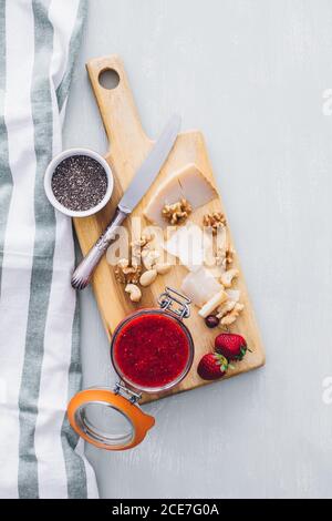 Von oben Blick auf den Tisch mit Erdbeermarmelade in einem Glas, Käse in Scheiben und Käse auf Holzbrett serviert Stockfoto