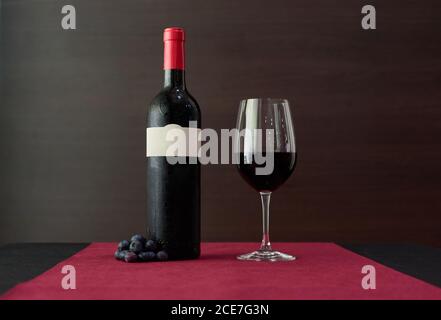 Ein Glas Rotwein und eine Flasche auf den Tisch gelegt mit Weintrauben im Luxusrestaurant Stockfoto