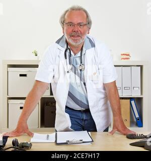 Der ältere Arzt steht hinter seinem Schreibtisch im des Arztes Büro Stockfoto