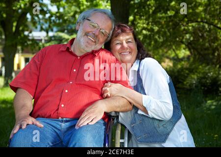 Lachende ältere Frau umarmt Mann in einem Rollstuhl in der parken Stockfoto