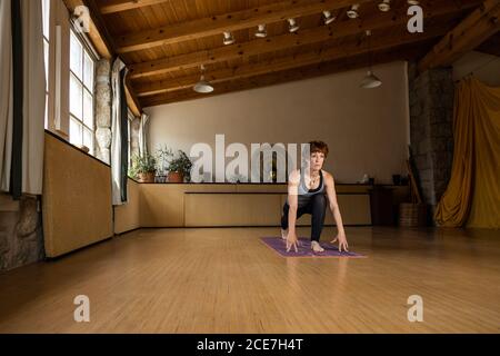 Rothaarige Frau, die in ihrem Holz- und Steinstudio auf ihrer Matte Yoga praktiziert, Seitenansicht Stockfoto