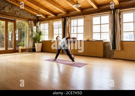 Flexible Frau in Sportbekleidung stehend in Triangle Pose in geräumig studio beim Yoga üben und aufschauen Stockfoto