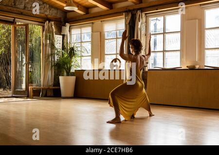 Rückansicht einer unerkennbaren ruhigen Frau, die barfuß auf Holz steht Etage im Studio in Utkata Konasana und meditieren Stockfoto