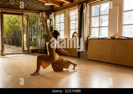 Seitenansicht einer fokussierten Frau, die barfuß im Studio steht Anjaneyasana und Yoga beim Aufschauen Stockfoto