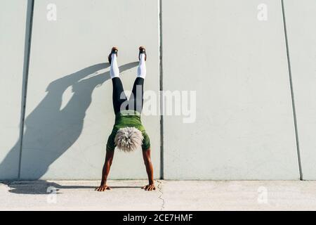 Rückansicht des unerkennbaren schwarzen Sportlers mit blonden Haaren Handstand in der Nähe der Wand des modernen Gebäudes in der Stadt Stockfoto