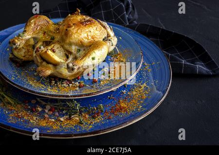 Von oben von Keramikplatten mit schmackhaftem französischem Coquelet mit goldene Oberfläche garniert mit Scheiben von gerösteten Kartoffeln und gewürzt Mit frischem Rosmarin und verschiedenen Gewürzen Stockfoto