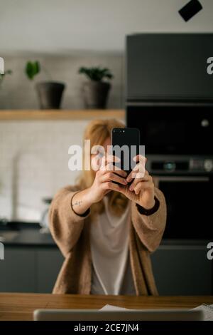 Frau, die am Tisch sitzt und Selfie mit dem Mobiltelefon nimmt Pause bei der Arbeit an entfernten Standorten zu Hause Stockfoto