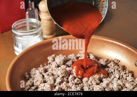 Anonyme Person Gießen hausgemachte Tomatensauce in Pfanne mit Gebratenes Hackfleisch beim Kochen Bolognese Sauce in der Küche Stockfoto