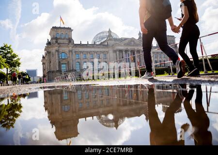 Berlin, Deutschland. August 2020. Ein Paar läuft an einer großen Pfütze des Regens entlang eines Schrankenzauens vor dem Reichstagsgebäude. Zwei Tage zuvor stürmten Demonstranten mit Reichsflaggen und rechtsextremistischen Schimpfungen auf die Treppe des Reichstags und nur drei Polizisten hielten die wütende Menge mit winkenden Schlagstöcken fern. Quelle: Christoph Soeder/dpa/Alamy Live News Stockfoto