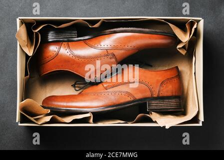 Braune Schuhe in einer Box auf schwarzem Hintergrund. Neue Schuhe aus echtem Leder in der Verpackung. Klassische Herrenschuhe. Draufsicht auf ein flaches Layout Stockfoto