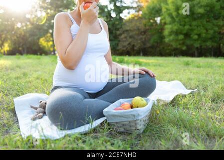 Nahaufnahme einer jungen Frau in Sportkleidung, die auf einer Trainingsmatte sitzt und beim Training im Freien frischen Apfel isst. Erwartet weibliche tun Yoga auf der Stockfoto