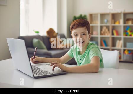 Schuljunge sitzt an einem Schreibtisch mit einem Laptop, schreibt Schulunterricht während der Hausaufgaben. Stockfoto