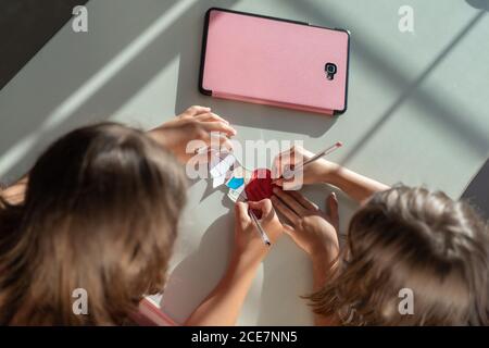 Von oben von unerkennbaren freundlichen Schwestern sitzen am Tisch in Zimmer und Malbild während unterhaltsam am am Wochenende Stockfoto