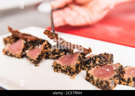 Nahaufnahme einer zugeschnittenen, nicht erkennbaren Person, die Thunfisch-Tataki verkleidet Platte Stockfoto