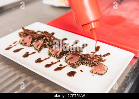 Nahaufnahme einer zugeschnittenen, nicht erkennbaren Person, die Thunfisch-Tataki verkleidet Mit Sauce auf einem weißen Teller Stockfoto