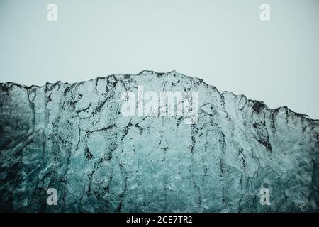 Strukturierte Oberfläche aus gefrorenem Eis mit Partikeln aus schwarzem Vulkanismus Sand gegen bewölkten Himmel am Diamond Strand der Jokulsarlon Lagune In Island Stockfoto