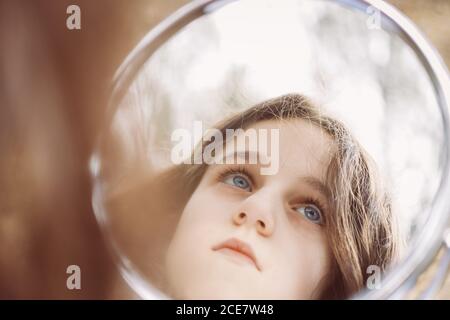 Wehmütig Kind mit blauen Augen und braunen Haaren wegschauen Beim Reflektieren in runden Spiegel in der Wohnung bei Tageslicht Stockfoto