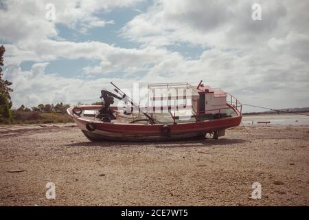 Altes motorisiertes Boot, das an einer sandigen Küste mit schäbiger Oberfläche gestrandet ist In der Nähe von Wasser und Bäumen unter dem Himmel mit niedrigen Wolken in Tageslicht Stockfoto