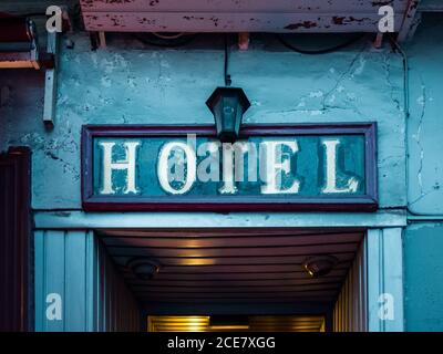 Rechteckige blaue Beschilderung mit Wort Hotel mit weißen Buchstaben geschrieben Und über verwitterten ländlichen Gebäudeeingang in der Nähe gemütliche Lampe platziert Stockfoto