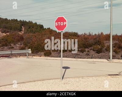 Rundes rotes Straßenschild mit Wort Stop auf leer Asphaltstraße in trockenem ländlichen Gelände Stockfoto