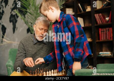 Großvater und Enkel setzen hölzerne Schachfiguren auf Schachbrett, die sich zum Spielen vorbereiten. Stockfoto