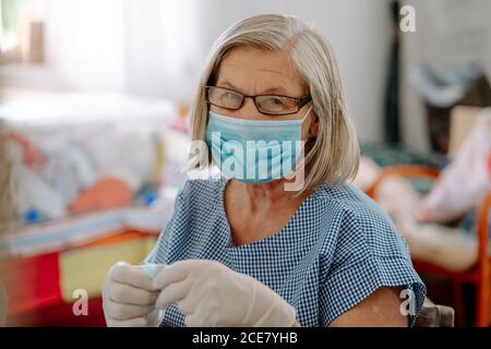 Handwerker in Latexhandschuhen, die ein Stück Stoff halten, während sie handgefertigte Masken für die Coronavirus-Prävention am Arbeitsplatz herstellen, wobei die Nähmaschine die Kamera anschaut Stockfoto