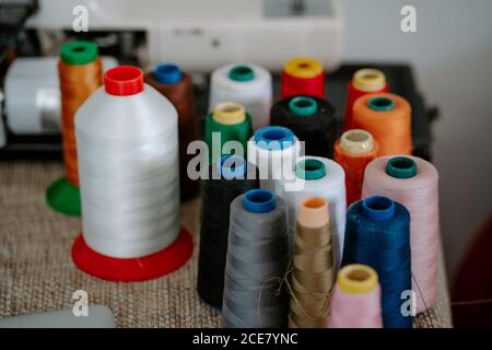 Der hohe Winkel der verschiedenen bunten Baumwollfäden auf den Spulen angeordnet Auf dem Tisch neben der Nähmaschine am Arbeitsplatz der Näherin Stockfoto