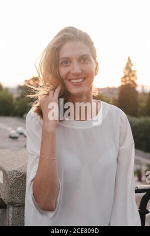 Erfreut positive Frau in weißer Bluse ruht auf der Straße Geländer Und die Kamera während der Sonnenuntergangszeit glücklich betrachten Stockfoto