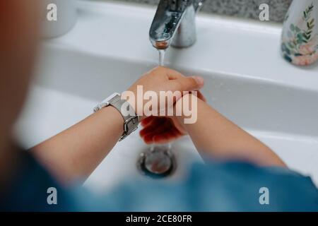 Von oben beschnitten unkenntlich kleines Kind Hände waschen in Waschbecken Im gemütlichen Badezimmer zu Hause Stockfoto