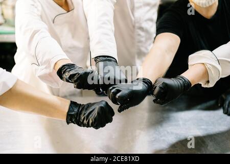 Beschnittene unerkennbare Inhalte Köche Team tragen Uniform und Handschuhe auffällig Handeln Sie mit Fäusten, während Sie in der modernen Restaurantküche arbeiten Coronavirus-Epidemie Stockfoto