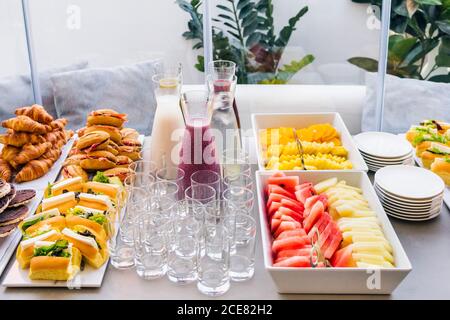 Hoher Winkel von sortierten Smoothie in Glasflaschen ein schmackhaftes Sandwiches mit Speckscheiben und süßen Croissants Tisch mit leeren Gläsern für Party Stockfoto