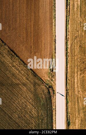 Von oben Luftaufnahme der geraden Straße durch landwirtschaftliche Feld im ländlichen Raum im Sommer Tag als Mann Geht die Straße hinunter Stockfoto
