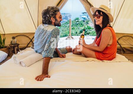 In voller Länge glücklich reifen Paar in casual Sommer tragen sitzen Auf dem Bett in Luxus-Camping-Resort und Blick auf jeden Andere mit Zärtlichkeit Stockfoto