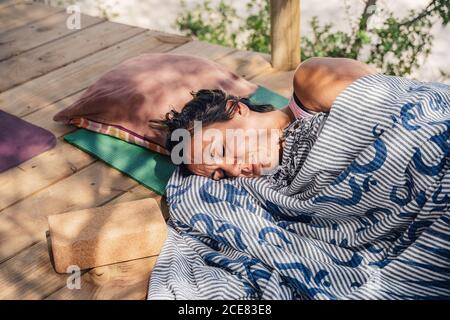 Von oben eine Frau mittleren Alters, die nach dem Yoga-Unterricht im Freien auf einer Matte im Garten schlief Stockfoto